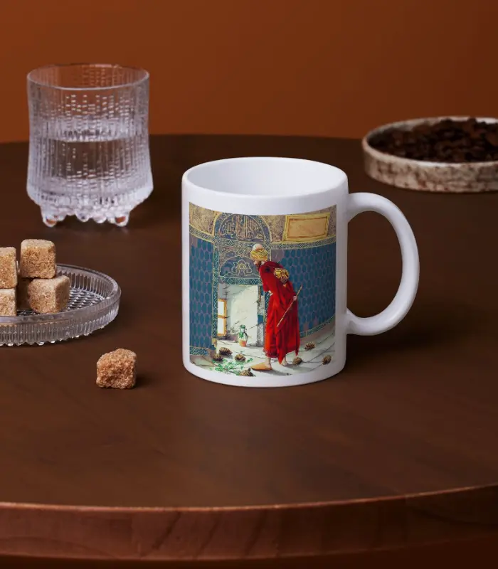 Kaplumbağa Terbiyecisi Tasarımlı Kupa Bardak, üzerinde kaplumbağa terbiyecisi sanatı olan beyaz seramik bir kupa - kırmızı cübbeli bir adam süpürüyor - kahverengi bir masanın üzerinde su, kahverengi küp şeker ve kahve çekirdeklerinin yanında duruyor.