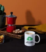 Beyaz bir kupa üzerinde yeşil bulut simgesi ve yazı ile birlikte, yanında cezve ve şeker küpleri bulunan bir masa düzeni. Sende kendi kupanı tasarlyabilirsin.