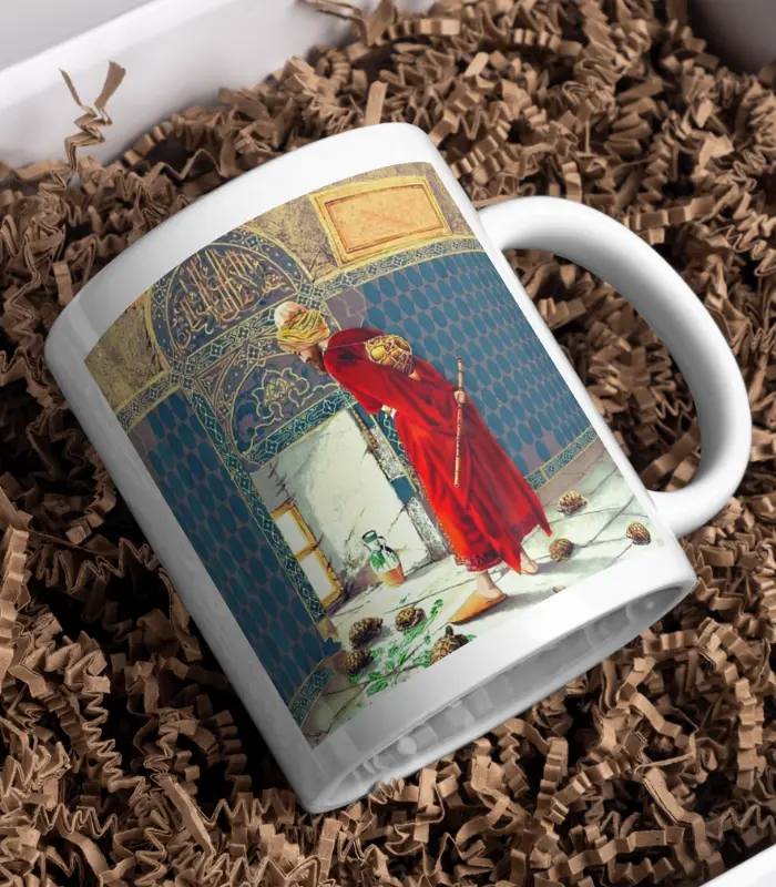 Kaplumbağa Terbiyecisi Tasarımlı Kupa Bardak, süslü bir camide dua eden kırmızı cübbeli bir figürün resmedildiği, çam kozalakları ile çevrili ve parçalanmış kahverengi kağıt üzerinde sergilenen beyaz bir kupadır.